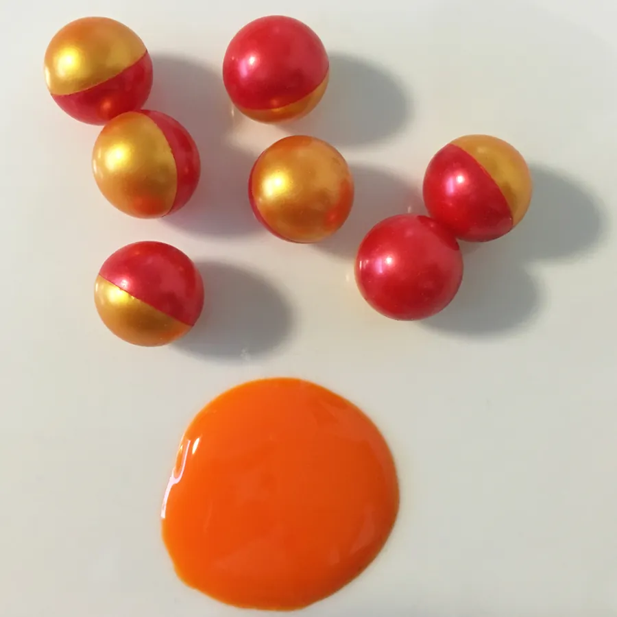 Paintballs Blast Premium bicolor rojo y dorado junto a una mancha de pintura naranja